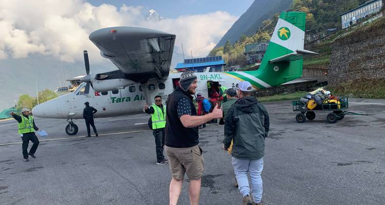 Menschen und ein kleines Flugzeug an einem Flughafen in der Nähe von Bergen.