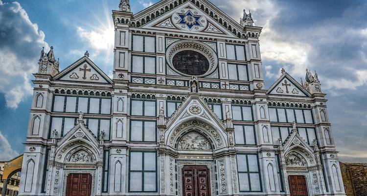 Fachada de mármol gótico de la Basílica di Santa Croce en Florencia, iluminada dramáticamente por la luz solar filtrada.