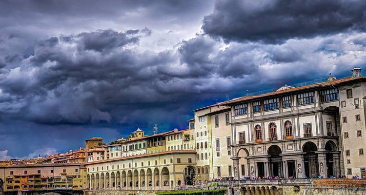 Edificios históricos junto al río con arcos en Florencia bajo unas nubes de tormenta dramáticas y oscuras.
