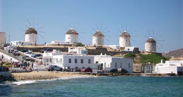 Iconic row of white windmills standing above whitewashed buildings on a Greek island waterfront.