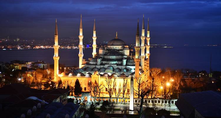La Mezquita Azul iluminada elevándose sobre Estambul al atardecer con el Bósforo al fondo.