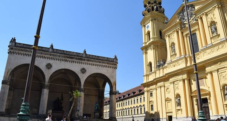 Historische gelbe Kirche und offene Loggia an einem Stadtplatz.
