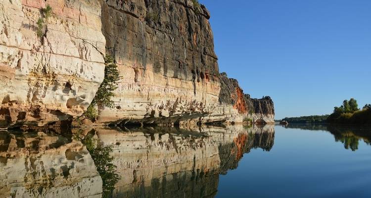 Kliffen die weerkaatsen in kalm water onder een heldere blauwe hemel.