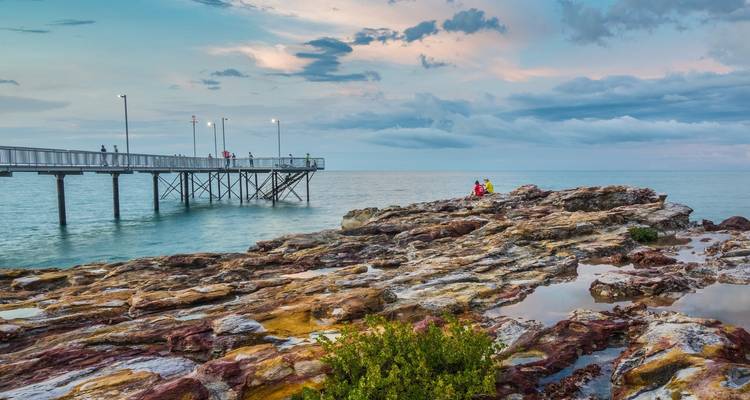 Steiger die zich uitstrekt in de zee met een rotsachtige kustlijn bij schemering.
