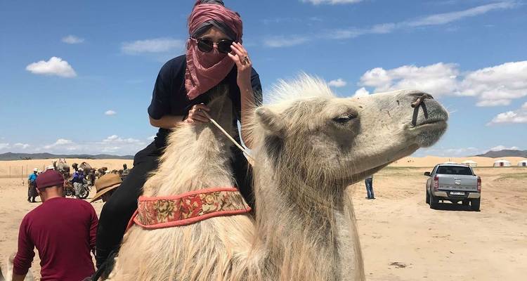 Person reitet auf einem Kamel in einer Wüstenlandschaft.