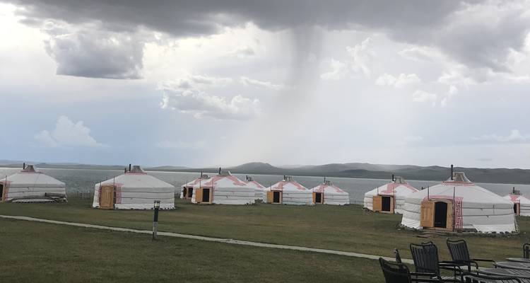 Jurten unter stürmischem Himmel in einer weiten offenen Landschaft.
