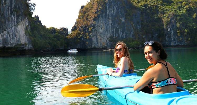 Mujeres sonrientes en kayaks con un telón de fondo de acantilados pintorescos.