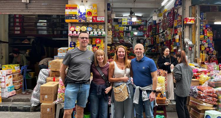 Des touristes posant dans un marché vietnamien animé entouré d'étagères de marchandises colorées.