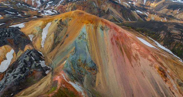 Aerial view of a streaked, multicoloured mountain slope accented with snow patches.