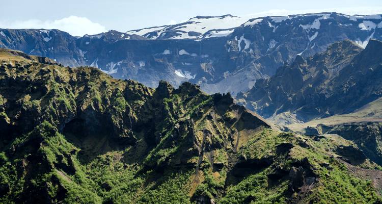 Crestas verdes dentadas y altos acantilados bajo un campo glaciar distante.
