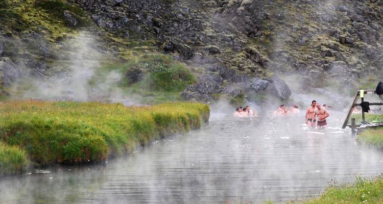 Bathers soak in a steaming natural river surrounded by mossy cliffs.
