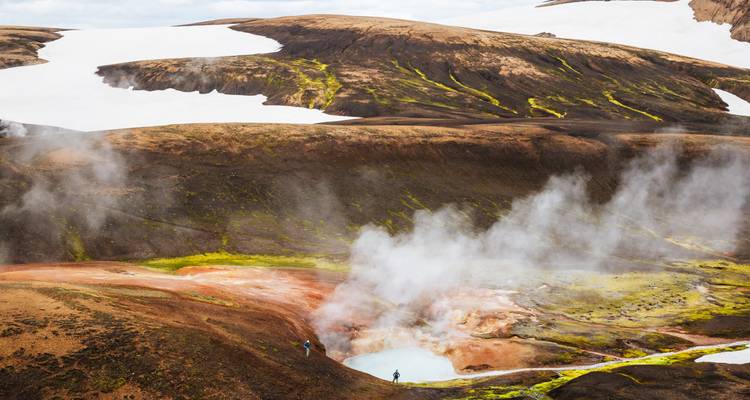 A steaming geothermal pool lies in a multicoloured volcanic basin edged by snow.