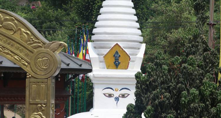 White stupa and ornate archway with colorful prayer flags in background.