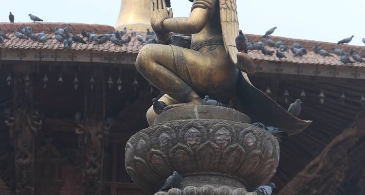 Golden statue surrounded by pigeons atop a pillar with ornate base.