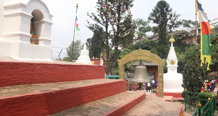 Temple complex with red brick steps, a bell, and people around.