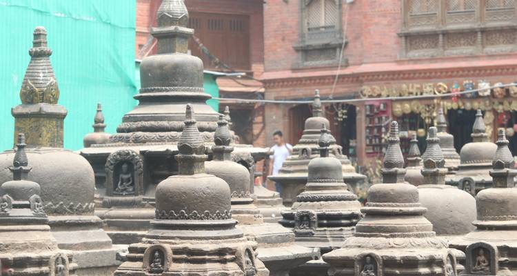 Stone stupas in front of traditional buildings, with people in background.
