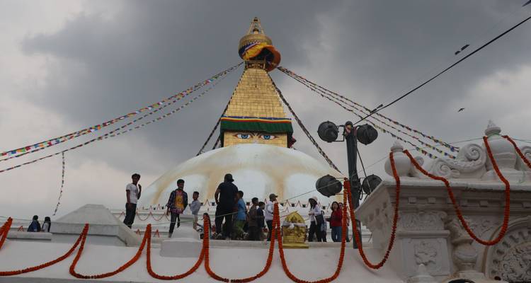 Stupa with colorful prayer flags and people around, under a cloudy sky.