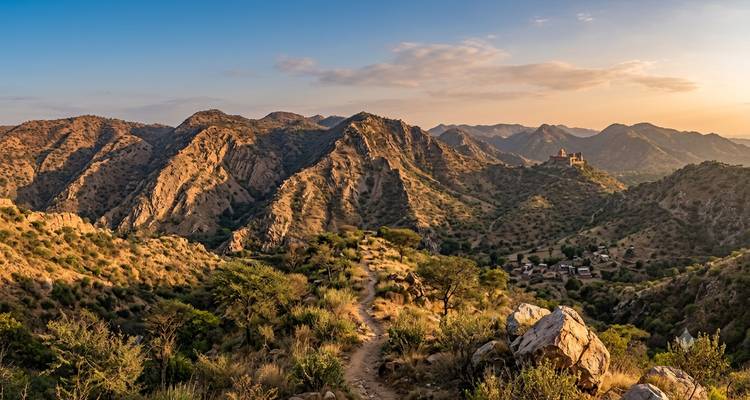 Warm evening light over the rolling Aravalli range with remote fort on a peak.
