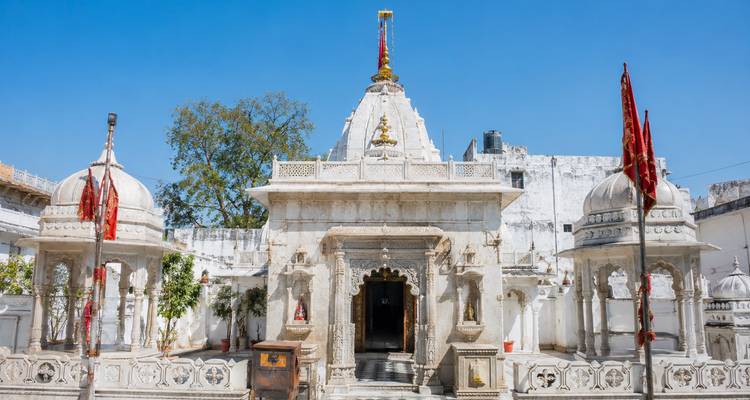 Un temple hindou immaculé en marbre blanc, orné de dômes, de drapeaux et de sculptures élaborées, se dresse sur un ciel bleu profond.