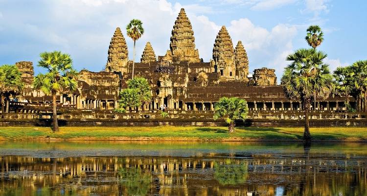 Iconic view of Angkor Wat with palm trees and reflection in the water.