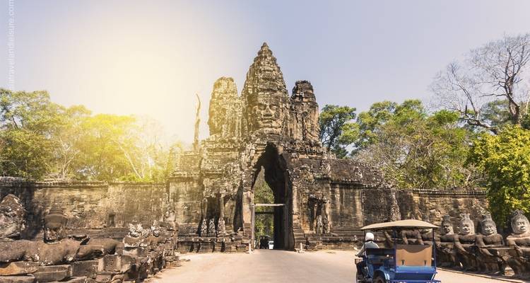 Stone tower gate with carved faces and people driving through it.