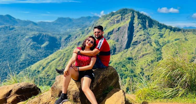 Pareja posando en un afloramiento rocoso con montañas frondosas.