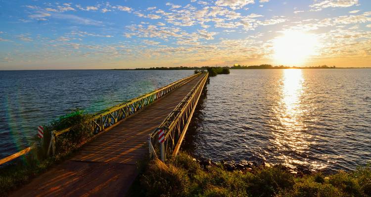 A long pier extending into a lake with a colorful sunset.