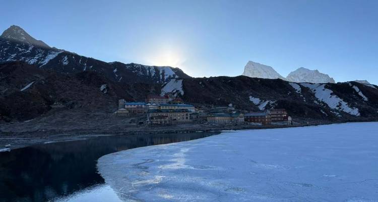El sol asoma sobre un lago alpino helado junto al pequeño pueblo de Gokyo al amanecer.