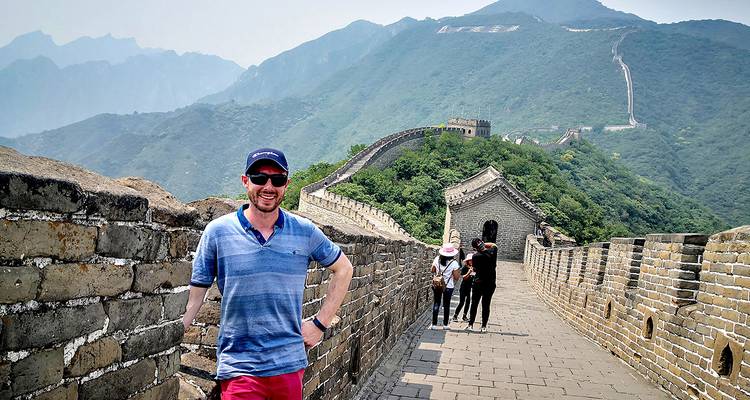 Man die poseert op de Chinese Muur met bergen op de achtergrond.