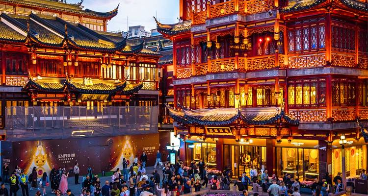 Los edificios iluminados por faroles tradicionales brillan en naranja sobre las multitudes ajetreadas en el bazar del Jardín Yu de Shanghai al atardecer.
