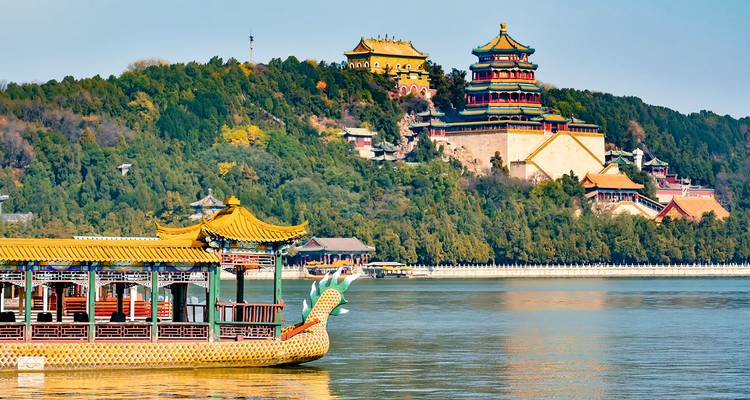 A dragon-head pleasure boat cruises Kunming Lake with the ornate Summer Palace rising on the wooded hill.