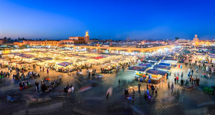 Le marché nocturne animé de Jemaa el-Fnaa scintille avec ses étals et ses foules sous le crépuscule bleu profond.