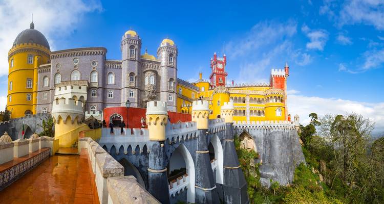 Les tours colorées et les créneaux du Palais de Pena se dressent au sommet d'une colline verdoyante sous un ciel qui s'éclaircit.