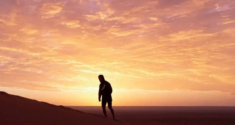 Silhouette eines einsamen Reisenden, der entlang einer Sanddüne gegen einen leuchtend orangefarbenen Himmel bei Sonnenuntergang geht.