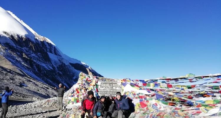 Groupe de personnes au col de Thorong La avec des drapeaux de prière et de la neige.