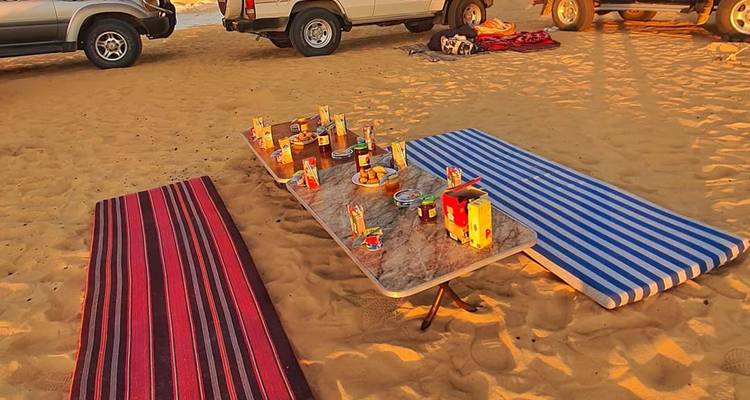 Wüstenpicknick-Aufbau mit Speisen auf einem Tisch und Matten rundherum.