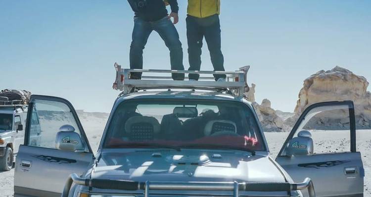Zwei Personen stehen auf einem SUV in einer Wüste mit offenen Türen.