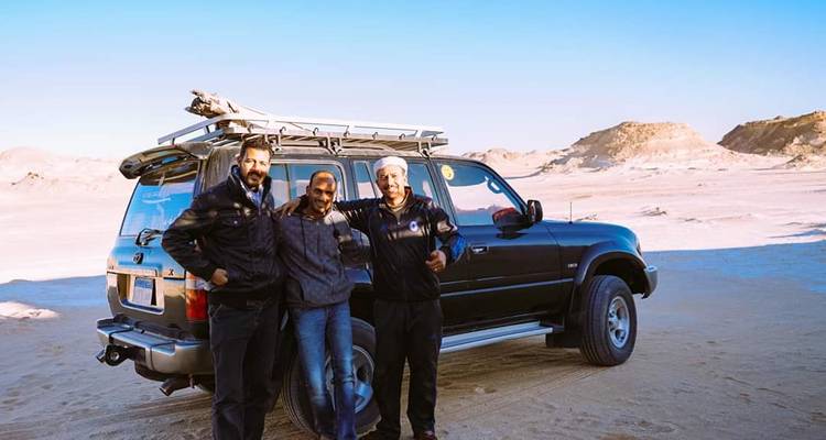 Drei Personen stehen vor einem geparkten SUV in einer Wüstenlandschaft.