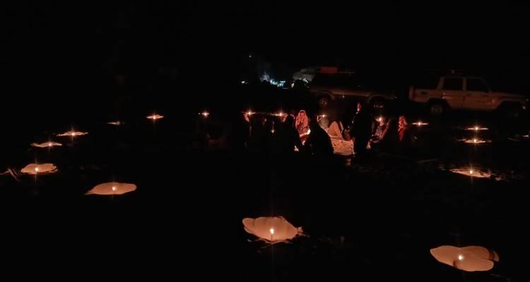 Menschen, die in einem Kreis mit Kerzen in der dunklen Wüste sitzen.