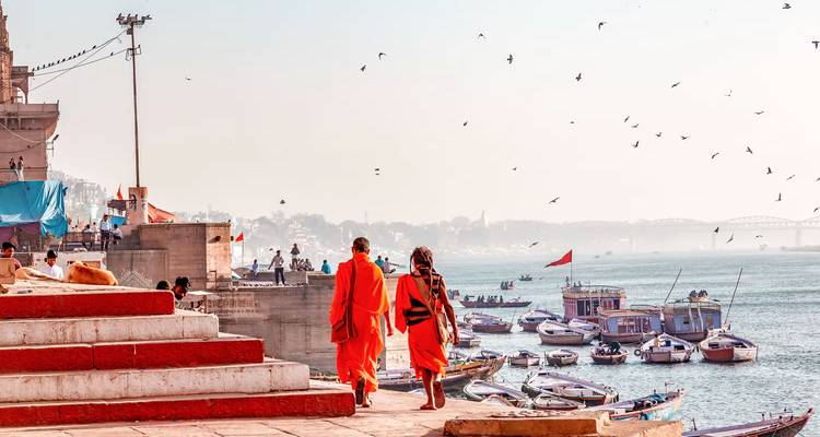 Two people in orange robes walking along the Ganges River.