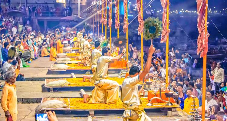 A vibrant religious ceremony taking place by the river with priests and a crowd of people.