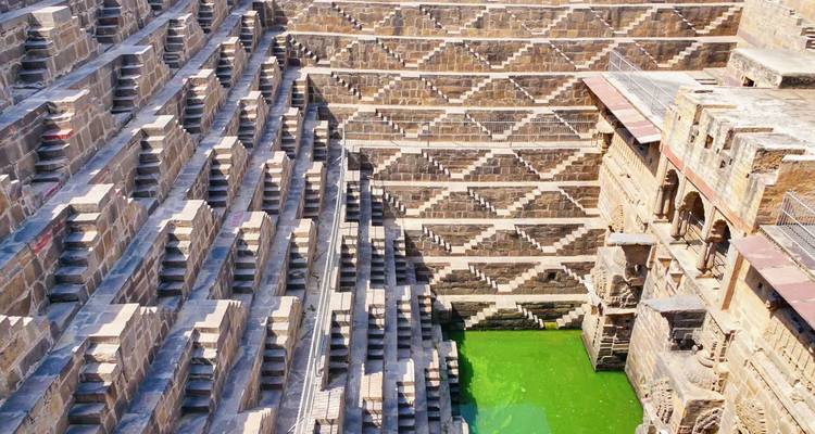 A stepwell with symmetrical stairs and green water at the bottom.