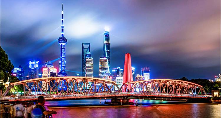 Dramatic night panorama of Shanghai’s illuminated skyline and bridge reflecting on the Huangpu River.