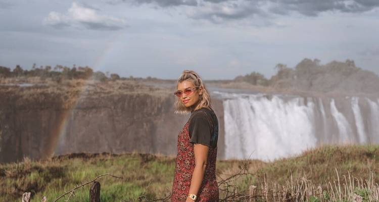 Woman posing in front of a waterfall with a rainbow.