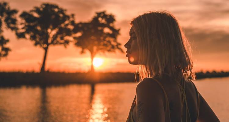 Femme regardant le coucher de soleil au-dessus d'une rivière.