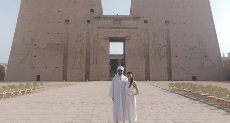 Paar posiert vor einer antiken Tempelmauer mit Schnitzereien.