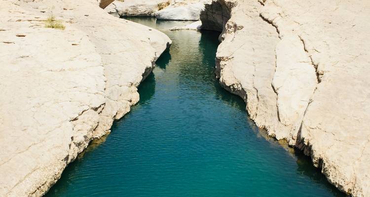 Schmaler türkisfarbener Wasserlauf zwischen felsigen Klippen.