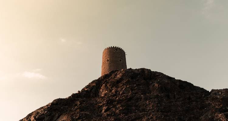 Historischer Turm auf einem felsigen Hügel vor dem Himmel.