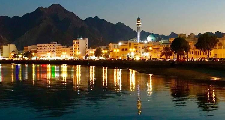 Stadsgezicht aan zee onder een sterrenhemel met verlichte gebouwen.