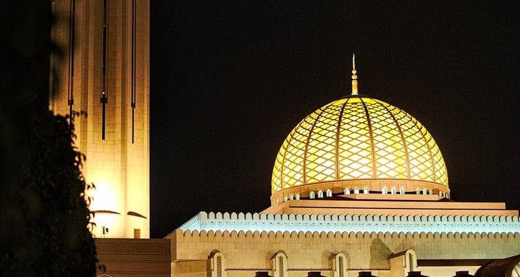 Helder verlichte moskeekoepel tegen een nachtelijke hemel.